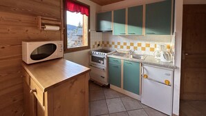 Een kleine keuken met houten kastjes, een magnetron, een fornuis en een spoelbak.