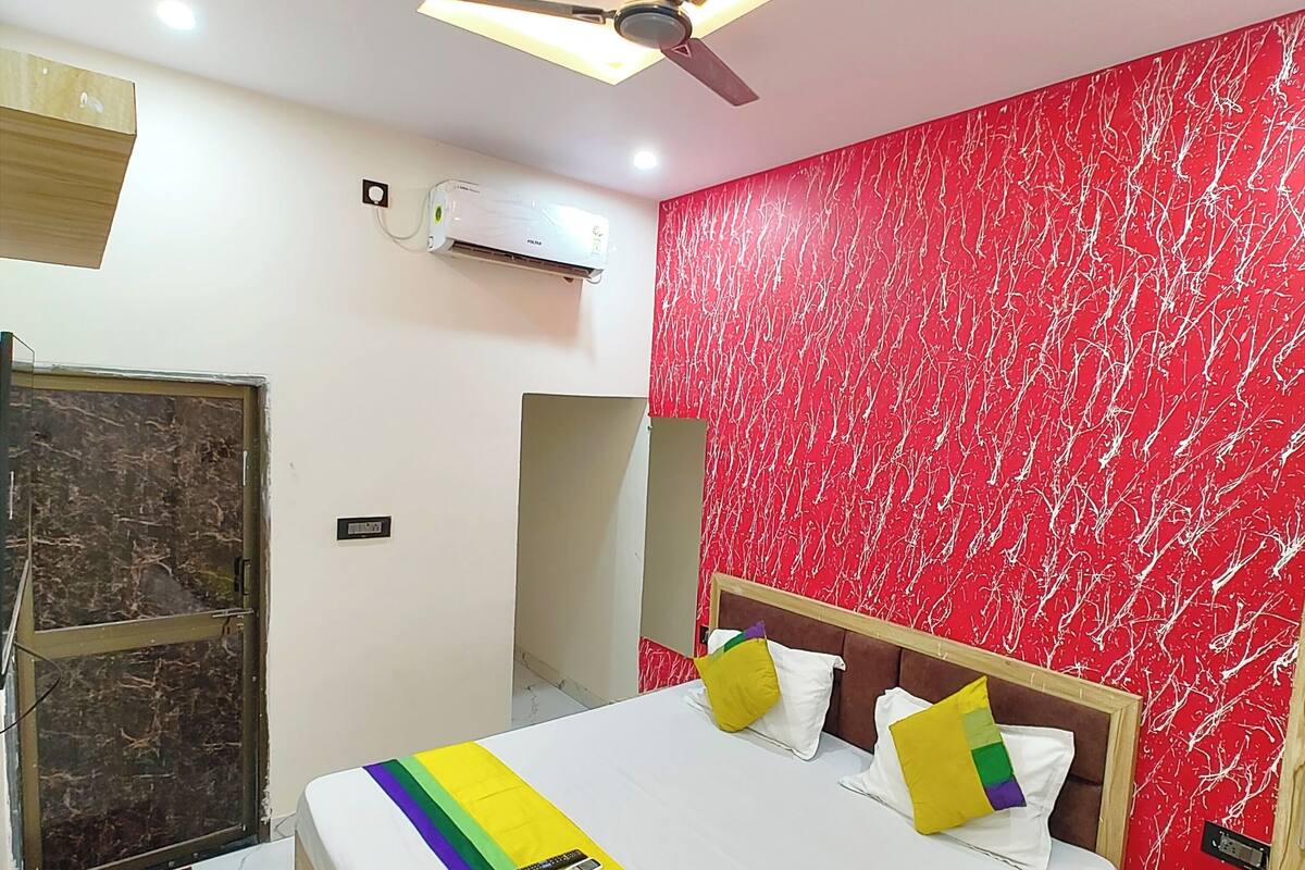 A hotel room with a bed, a ceiling fan, an air conditioner, and a red marble-patterned wall.
