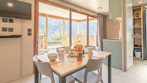 A dining area with a table set for two, a kitchen area with a stove, and a view of mountains through large windows. - Chalet for 4 near ski lifts, mountain view (Aussois)