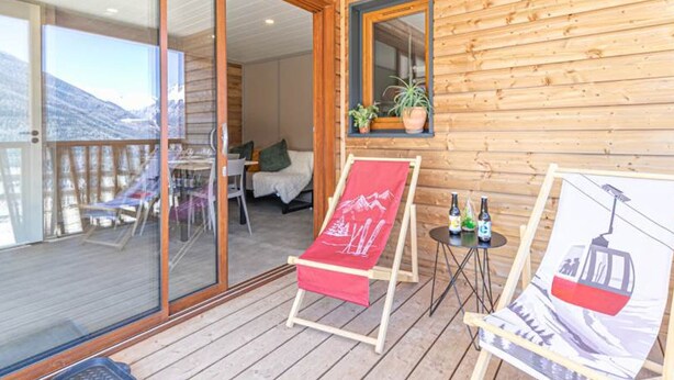 A wooden cabin with a balcony, a bed, a table with chairs, and a painting of a cable car. - Chalet for 4 near ski lifts, mountain view (Aussois)