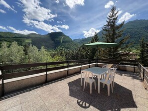 An outdoor patio with a table and chairs, a green umbrella, and a scenic mountain view.