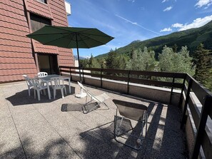 Una terrazza con tavolo e sedie, un ombrellone verde e vista su una montagna.