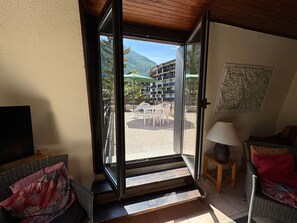 Una habitación con puerta corrediza de vidrio que da a un patio exterior con mesas y sillas, techo de madera y televisor a la izquierda.