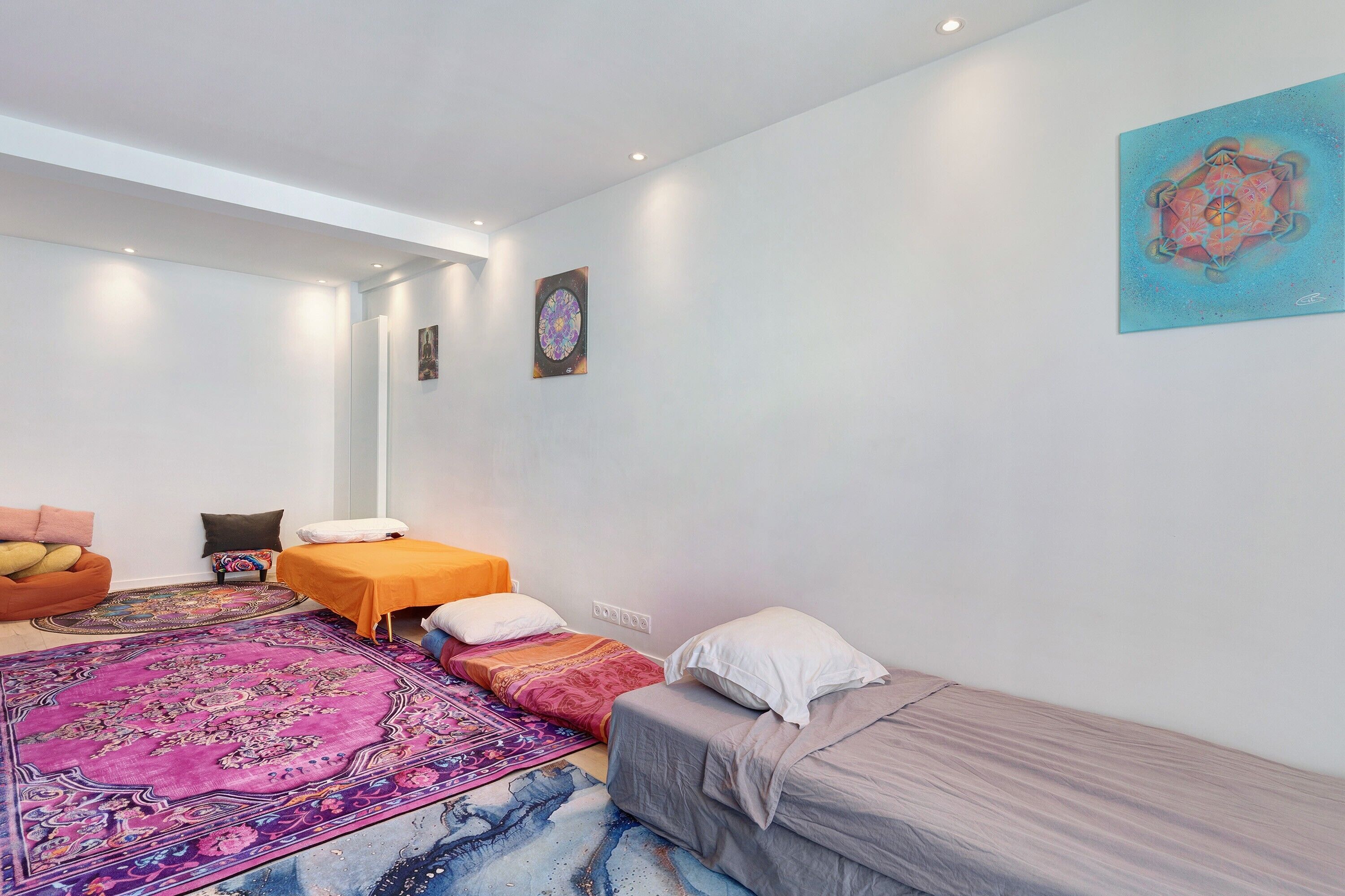 Quarto compacto com cama, sofá, mesinha e tapete colorido.