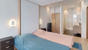 Una camera da letto con un letto, comodini, un armadio e un bagno parzialmente visibile da una porta aperta.