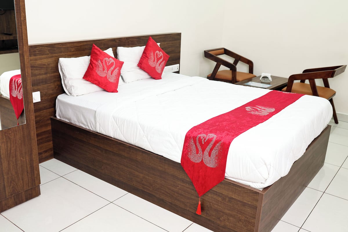 A neatly made bed with a red and white bedspread, a wooden headboard, and a small bedside table with a lamp.