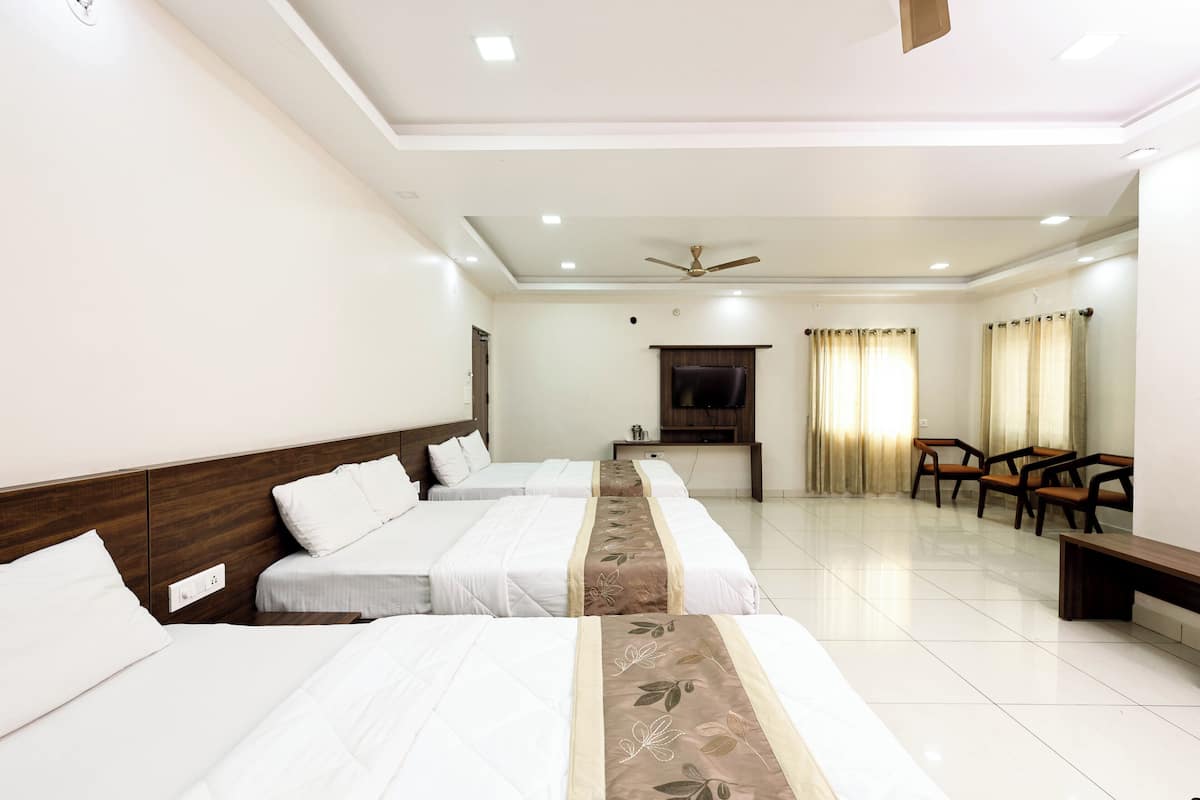 A hotel room with three beds, a ceiling fan, a TV, and a seating area with chairs.