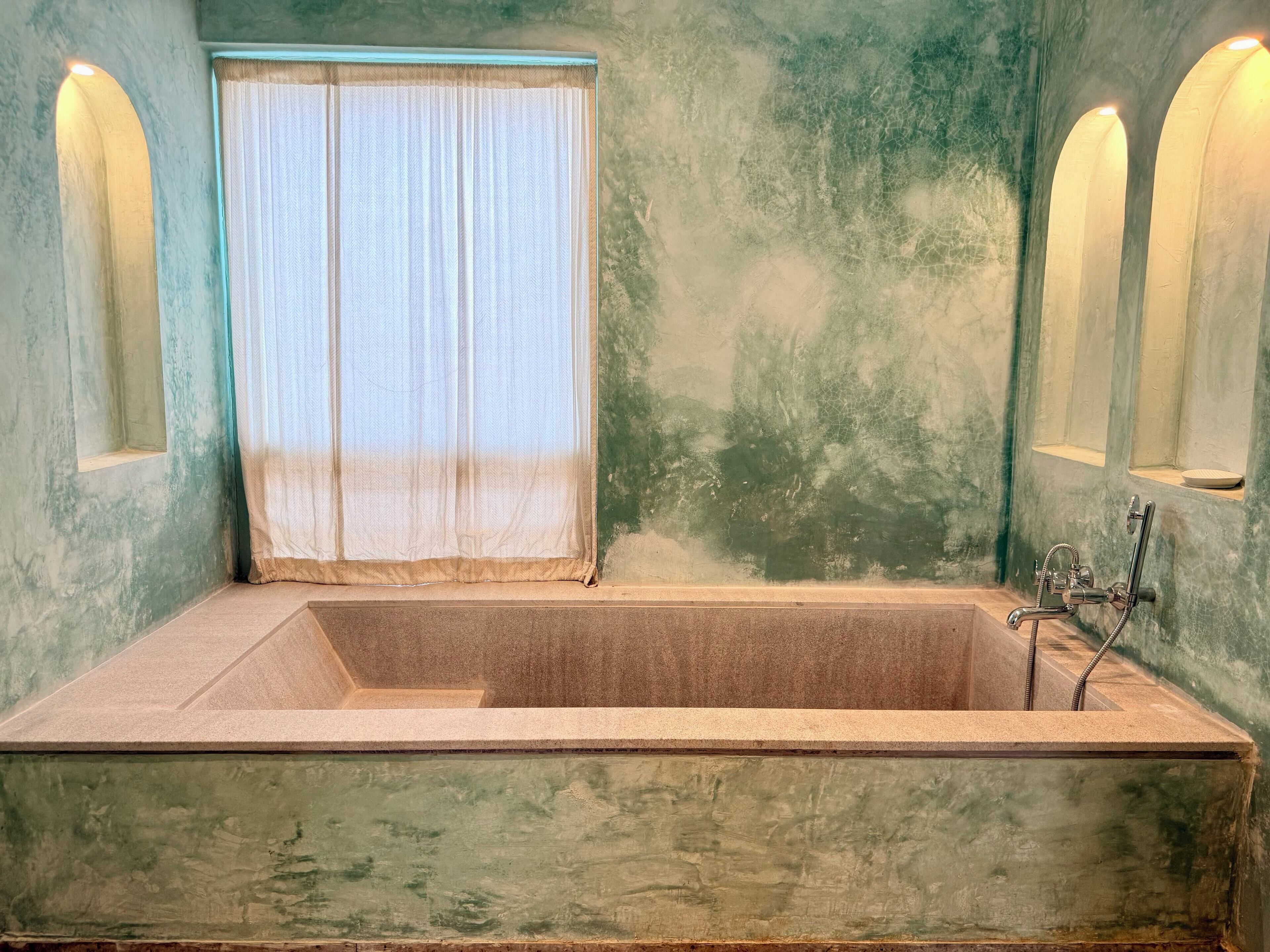 Una bañera rectangular con ducha, una ventana con cortina translúcida y dos luces empotradas.