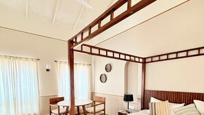 A four-poster bed with a wooden frame, a round wooden table, a chair, a desk, and a lamp. - Love Story by Purple Door Villas (Siolim)