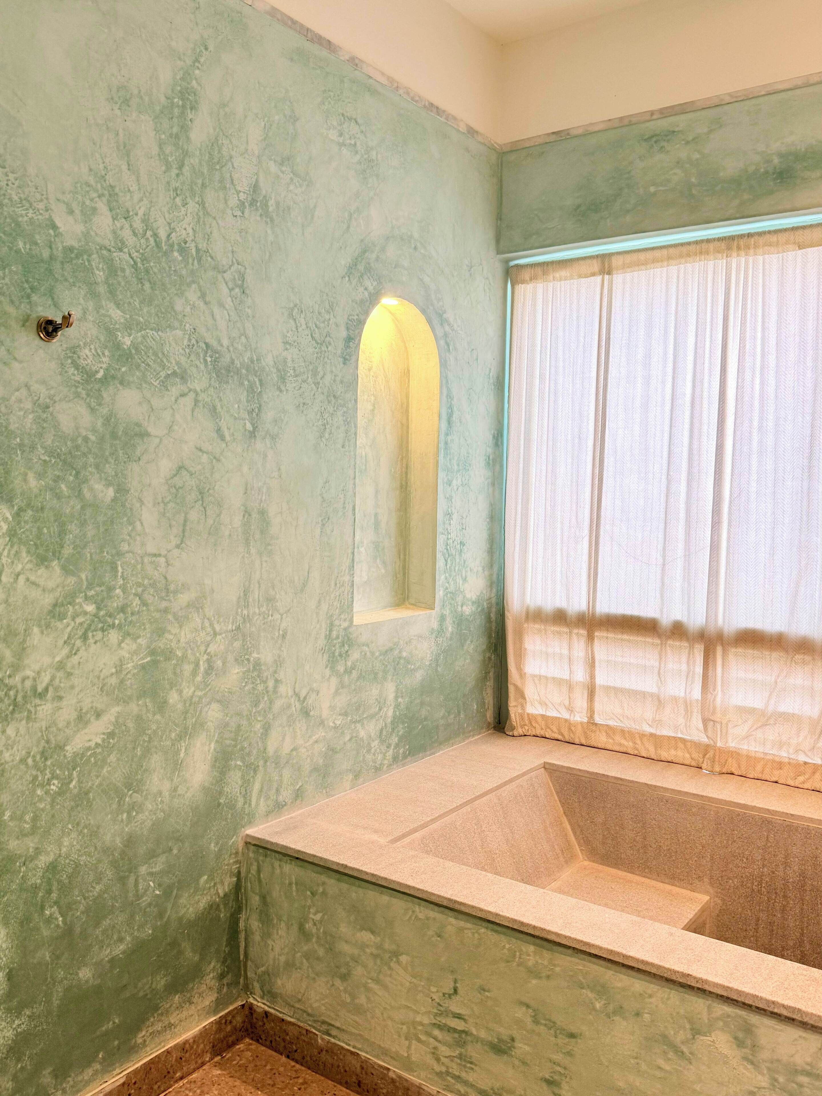 Ein Badezimmer mit Badewanne, einem Fenster mit Vorhängen und einer strukturierten Wand.