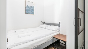 A single bed with white bedding, a small wooden table, and a framed picture on the wall. - RentPlanet - Fort Wola (Warsaw)