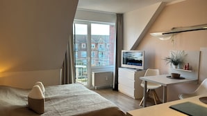 Habitació d'hotel moderna amb llit, escriptori, cadira, televisió i vista a edificis a la finestra.