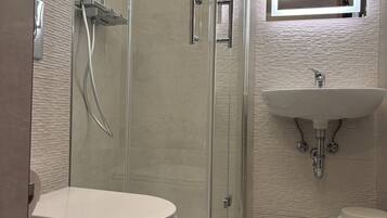 A modern bathroom with a glass-enclosed shower, a white toilet, and a sink with a mirror above it.