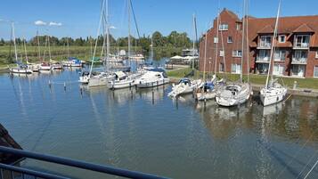 En lystbådehavn med flere sejlbåde i havnen, en murstensbygning med balkoner, og en klar blå himmel.