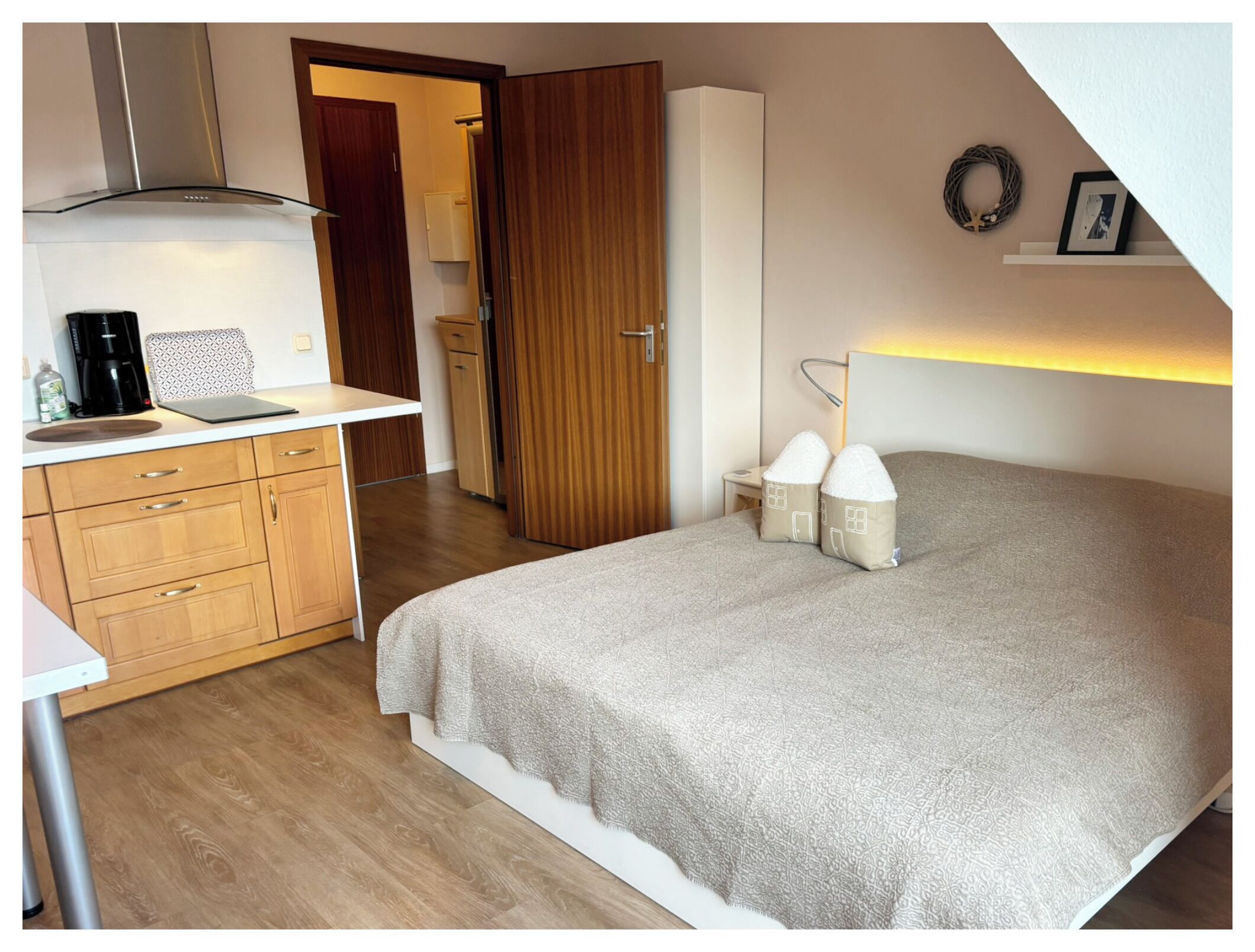 Ein Schlafzimmer mit Bett, Nachttischlampen, einem Schminktisch, einem Schreibtisch und einer Küchenzeile mit Herd.