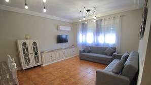 A living room with a grey sofa, a white cabinet, a flat-screen TV, and a chandelier. - El Balcon a Toledo 10 min from puy du fou (Cobisa)