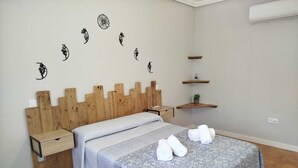 A bedroom with a wooden headboard, a patterned bedspread, a nightstand, a wall-mounted shelf with a plant, and a towel on the bed. - El Balcon a Toledo 10 min from puy du fou (Cobisa)