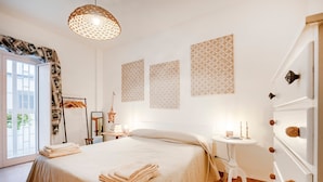 Une chambre à coucher avec un lit, une table de chevet, des éléments de décoration murale et une vue sur l’extérieur, visible à travers une porte.