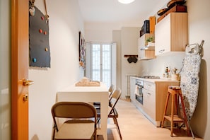 A compact kitchen with a dining area, wooden cabinets, and a small stool.