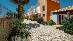 A row of modern, two-story houses with balconies, a cobblestone pathway, and a palm tree. - Jardins de Pera (Silves)