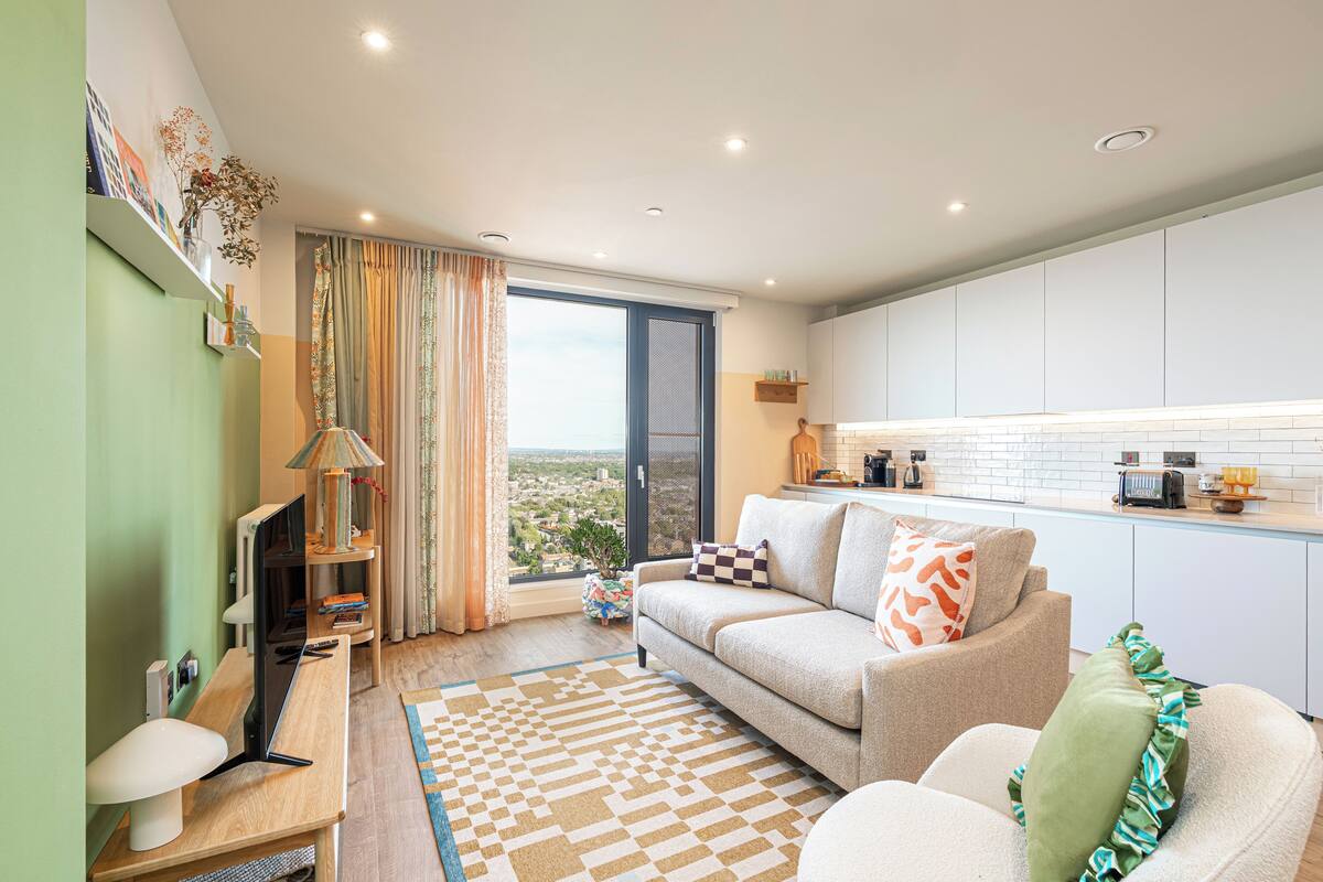 A modern living room with a sofa, a coffee table, a TV, and a view of the city through a large window.