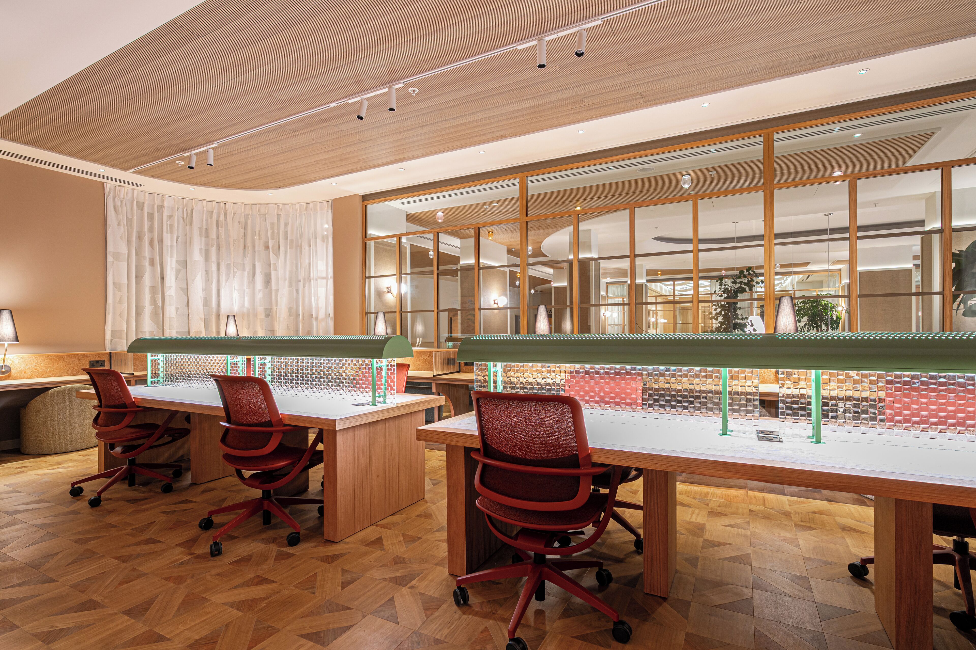 A conference room with wooden desks, red office chairs, and a large window with a view of the interior.