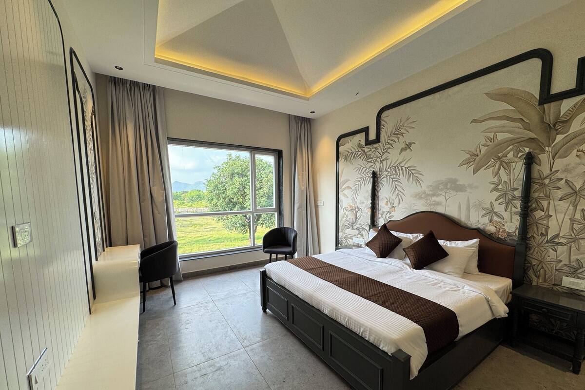 A modern bedroom with a large bed, a desk, and a view of a green landscape through a large window.