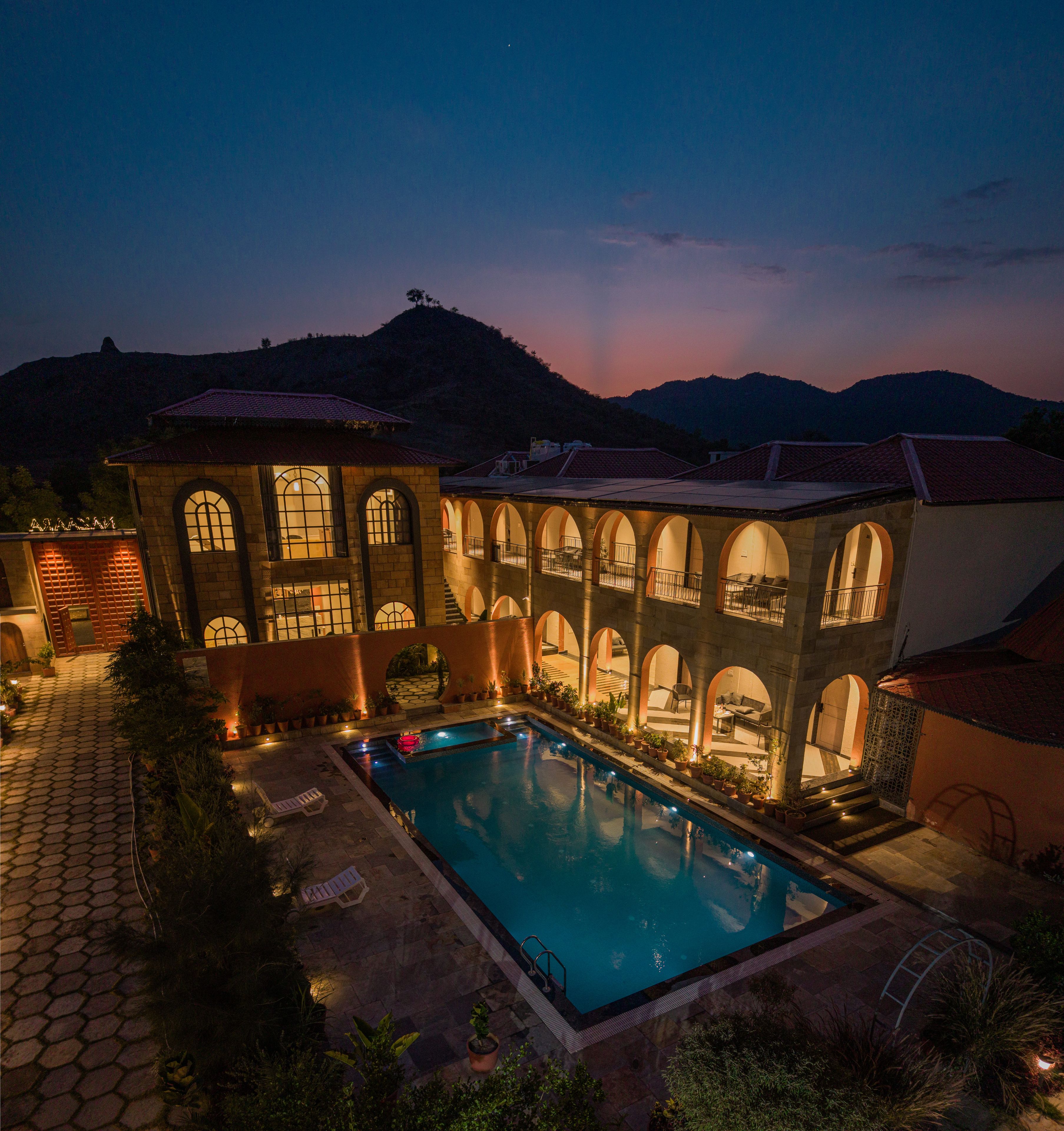 A poolside area with a swimming pool, a covered outdoor seating area, and a building with arched windows and balconies.