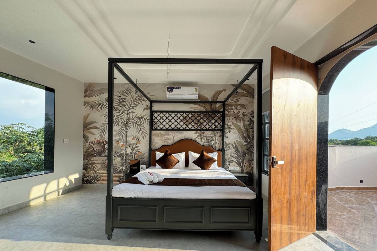 A four-poster bed with a wooden headboard, a decorative wall panel, and a view of greenery outside.