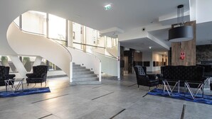 A spacious lobby with a curved staircase, black leather seating, and a modern chandelier. - SPV Apart Pileckiego 258 (Warszawa)