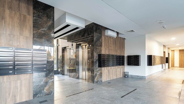 A modern lobby with a marble floor, wooden paneling, and a reception desk with a black panel. - SPV Apart Pileckiego 258 (Warszawa)