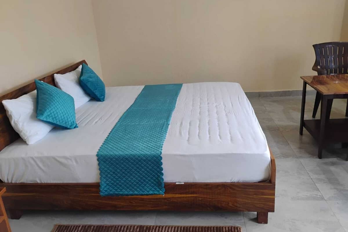 Una cama con estructura de madera, ropa de cama blanca y almohadas y una manta color turquesa.