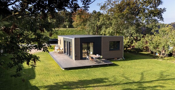 A modern, single-story house with a deck, surrounded by a well-maintained lawn and trees. - Vacation home LieblingsKOOG in Friedrichskoog (Friedrichskoog)