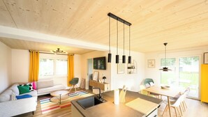 A modern kitchen with a central island, a dining area with chairs, a sofa, and a window with curtains.
