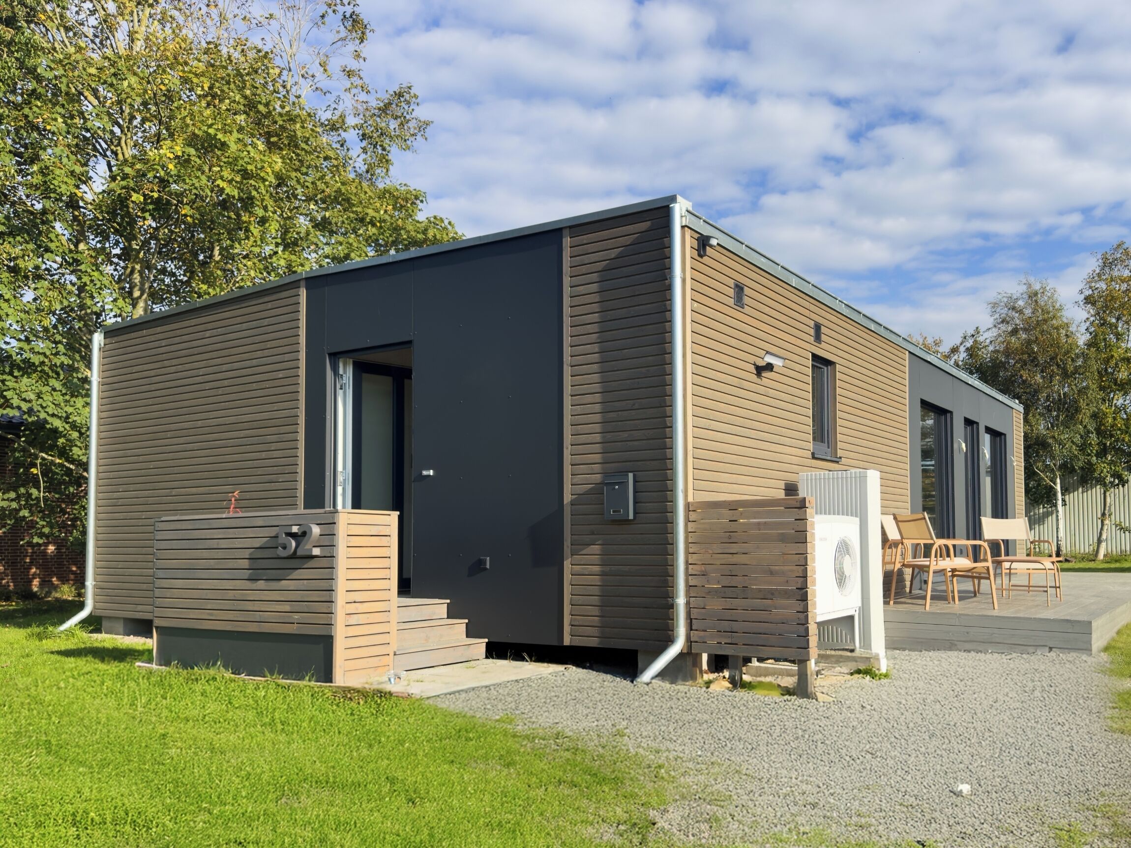 A modern, single-story building with a dark exterior and wooden accents. It features a small porch with outdoor seating and a visible number "52" on the side.