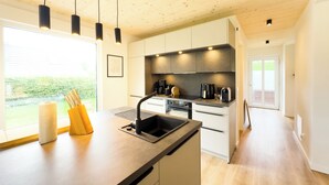 A modern kitchen with a wooden ceiling, a large window, and a view of the outdoors.