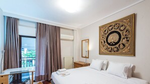 A hotel room with a bed, a desk, a chair, a window with curtains, a radiator, a mirror, and a decorative wall piece. - City Moon by halu (Thessaloniki)