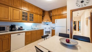 A modern kitchen with wooden cabinets, a microwave, a coffee maker, a sink, and a dining area with a table and chairs. - City Moon by halu (Thessaloniki)