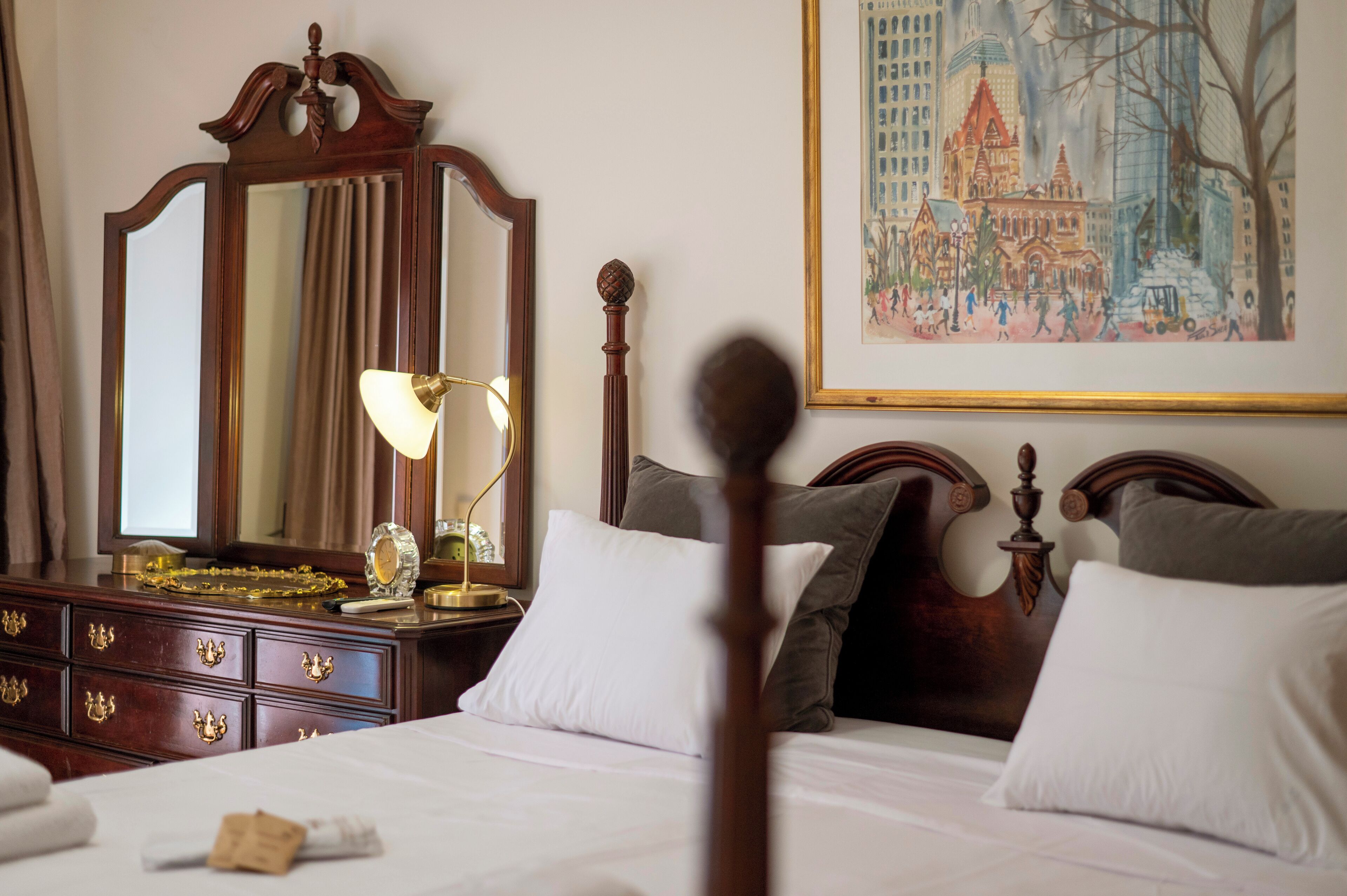 Une chambre d’hôtel avec un grand miroir, une lampe de chevet, une tête de lit en bois et un tableau au mur.
