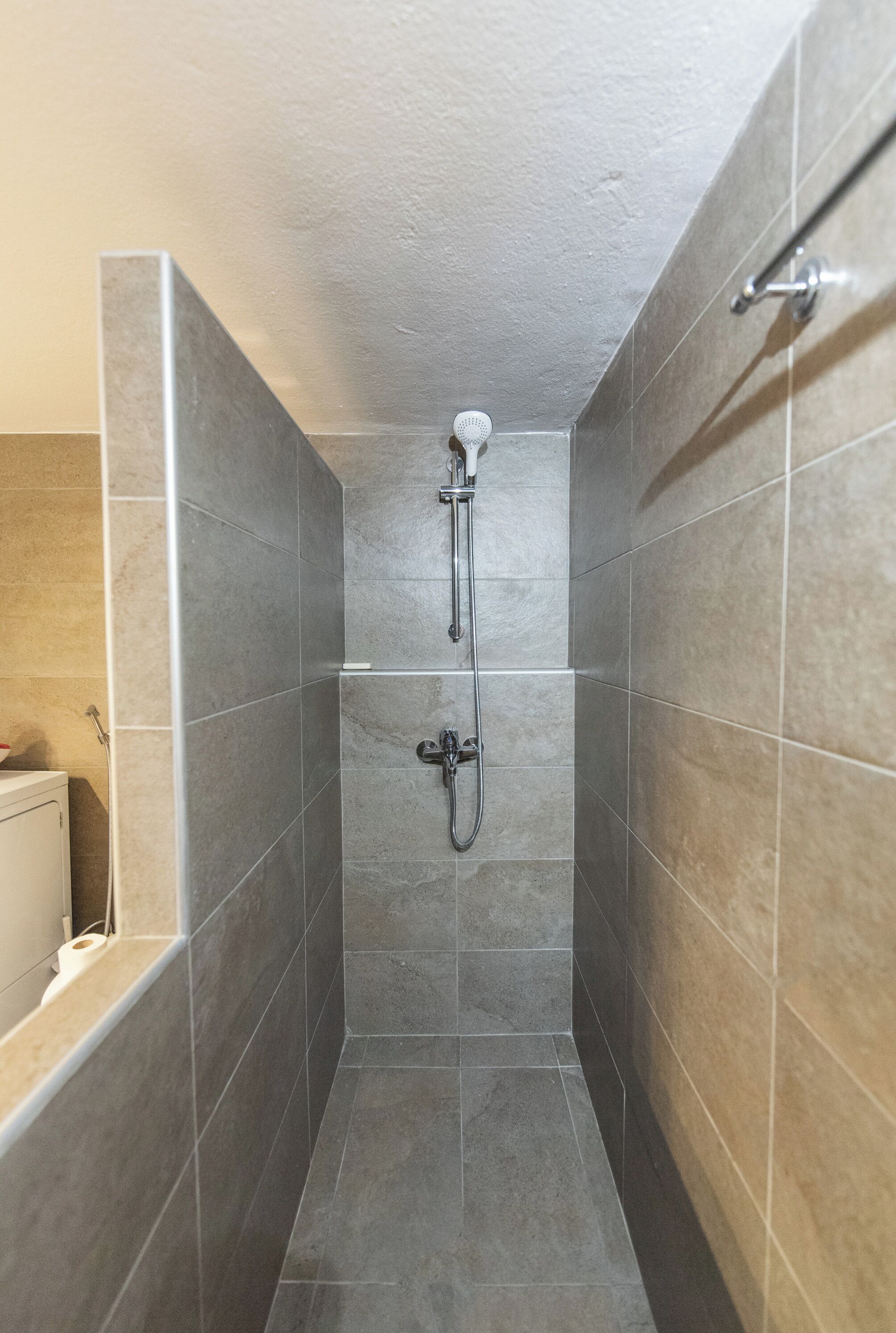 A narrow shower stall with a handheld showerhead and a wall-mounted faucet.