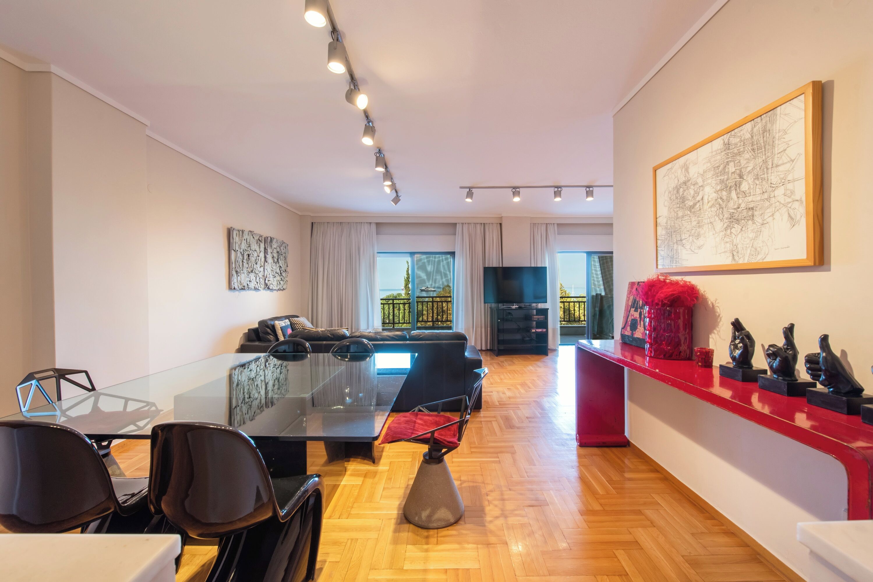 Una sala de estar moderna con una mesa de comedor de vidrio, sillas negras, un sofá y una pared roja decorativa con adornos.