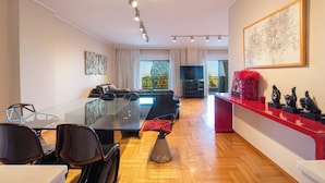 A modern living room with a glass dining table, black chairs, a sofa, and a red accent wall with decorative items. - City Moon by halu (Thessaloniki)