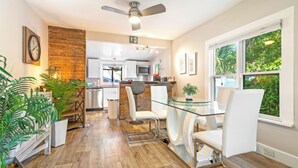 Une cuisine moderne avec des meubles blancs, un four à micro-ondes en acier inoxydable et un coin repas comprenant une table en verre et des chaises blanches.