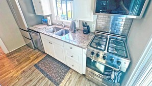 Une cuisine moderne avec des armoires blanches, un réfrigérateur en acier inoxydable, un évier à deux bacs, une cuisinière et un four à micro-ondes.