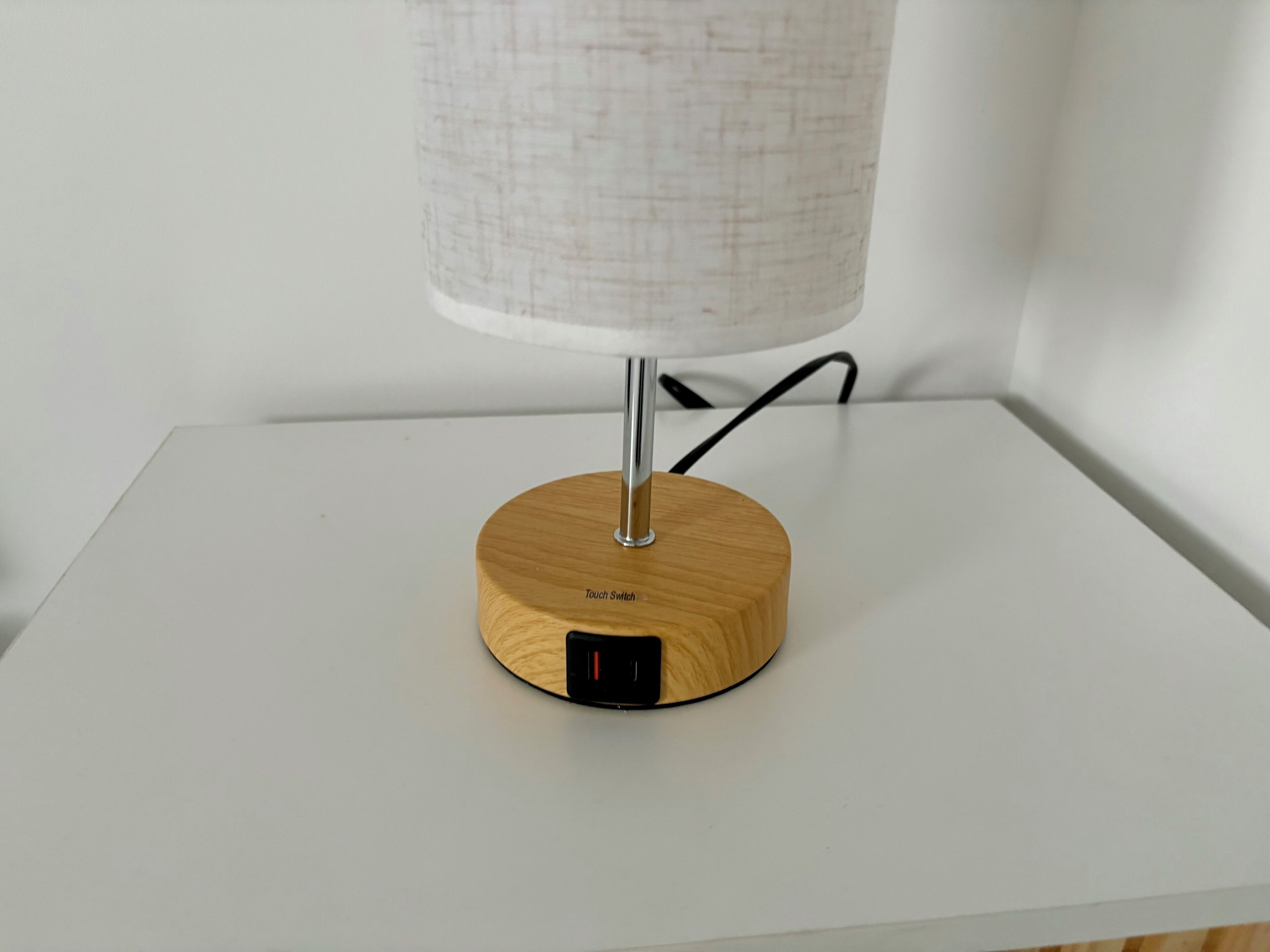 A modern lamp with a wooden base and a touch switch on a white table.
