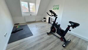 A spacious room with a wooden floor, a black exercise bike, and a yoga mat.