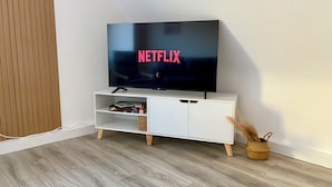 A modern living room with a flat-screen TV displaying the Netflix logo, a white entertainment unit, and a woven basket on the floor.