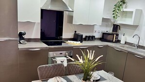 Une cuisine moderne équipée d’appareils électroménagers en acier inoxydable, un coin repas avec une table dressée pour deux personnes et une plante en pot posée sur le comptoir.