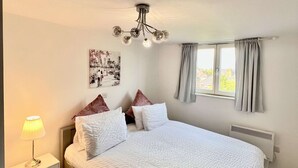 Un lit bien fait, avec du linge de lit blanc, une lampe de chevet et un tableau accroché au mur.