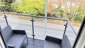 L'intérieur d'un autobus, avec une rambarde en métal, deux fauteuils en osier et une vue sur une rue résidentielle bordée de maisons et d'arbres.